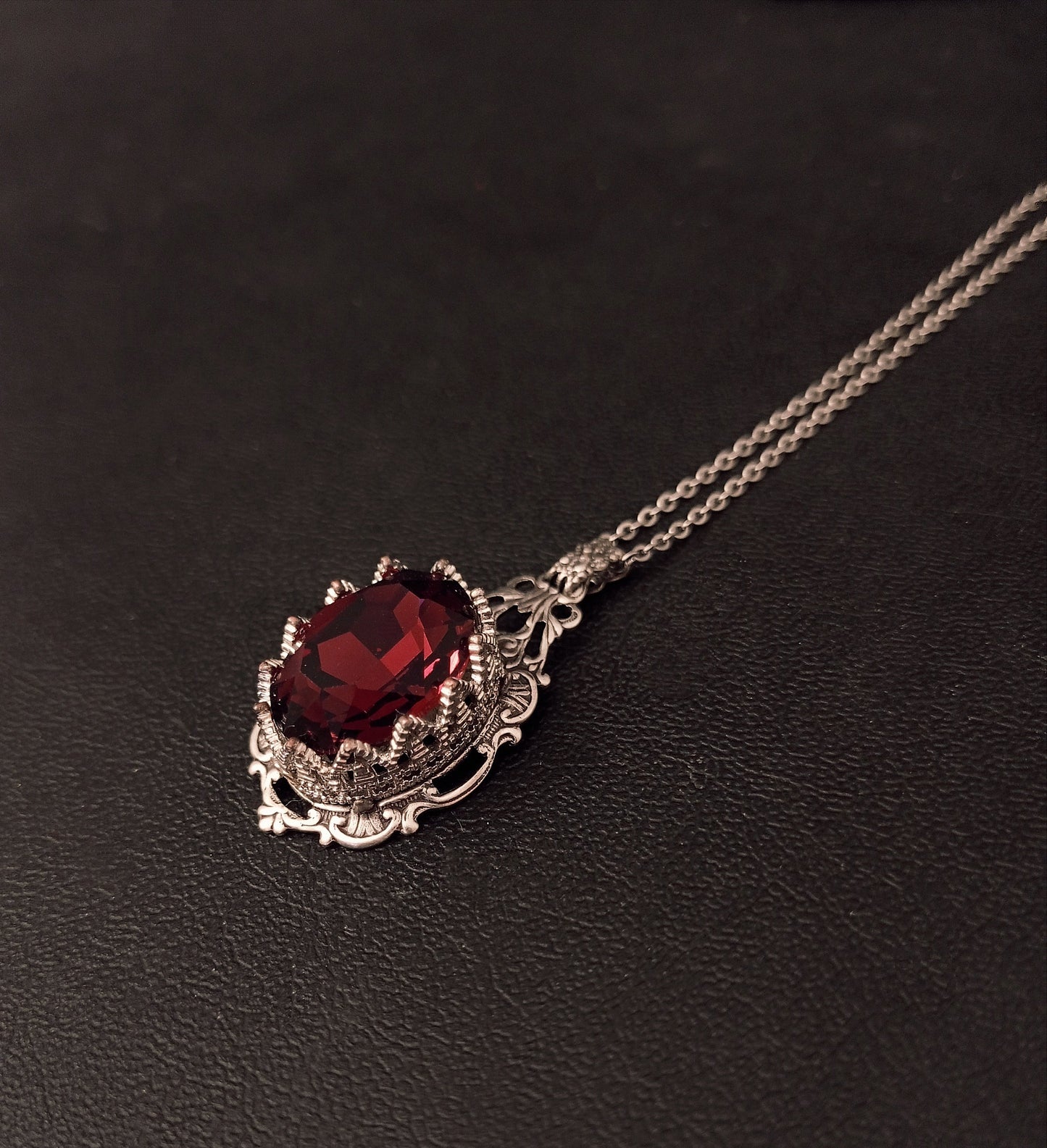 Ornate necklace showcasing a beautiful dark red gem in intricate silver setting.