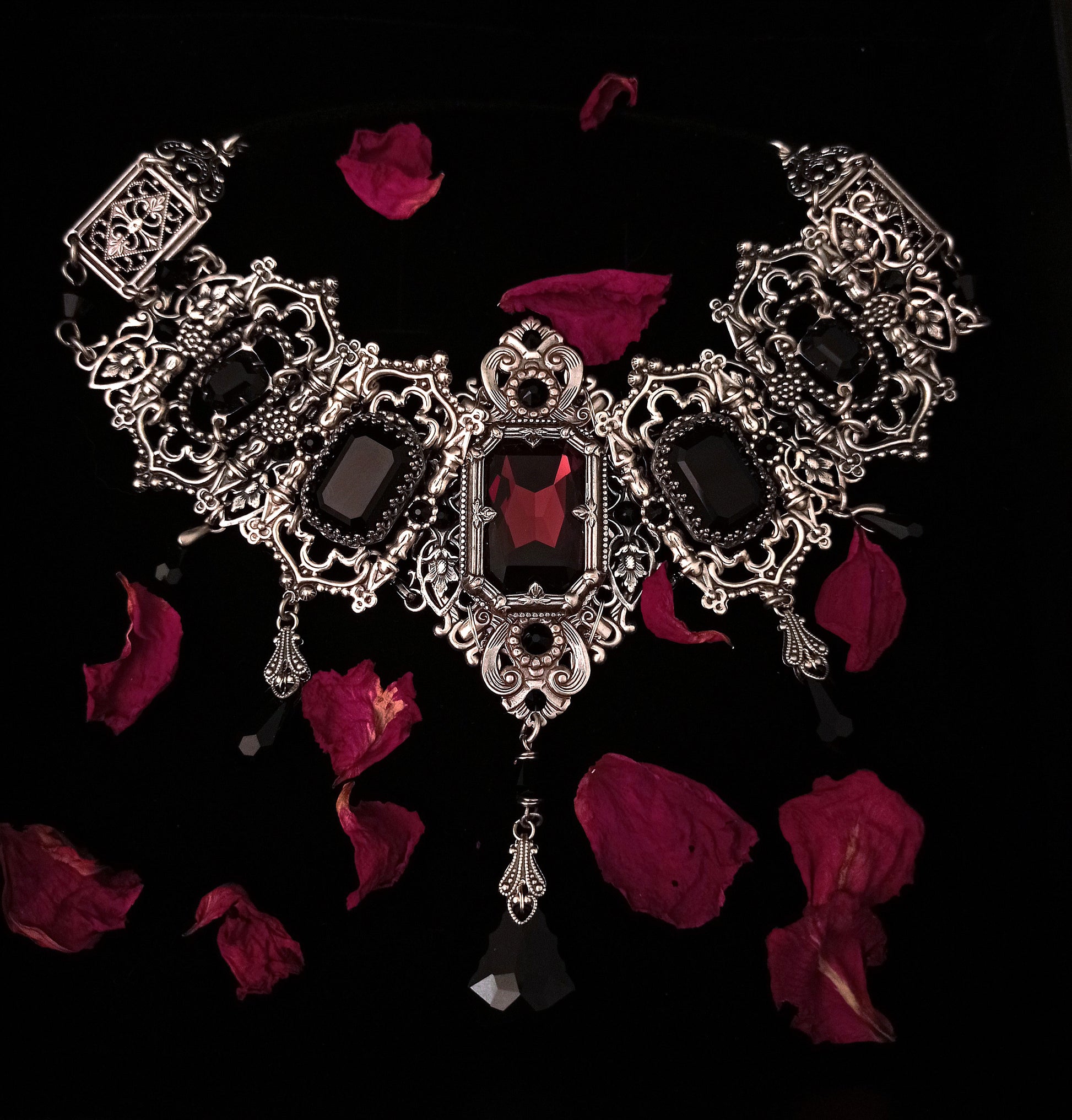 Most grand riviere gothic choker with intricate silver accents, a focal Burgundy stone and smaller black ones.
