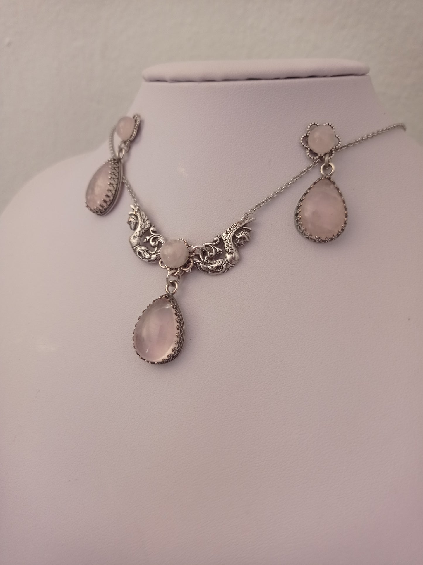 Rose Quartz necklace and earrings set featuring ornate detailing and matching pink teardrop-shaped stones. The set includes drop earrings and a necklace with three stones in decorative frames.