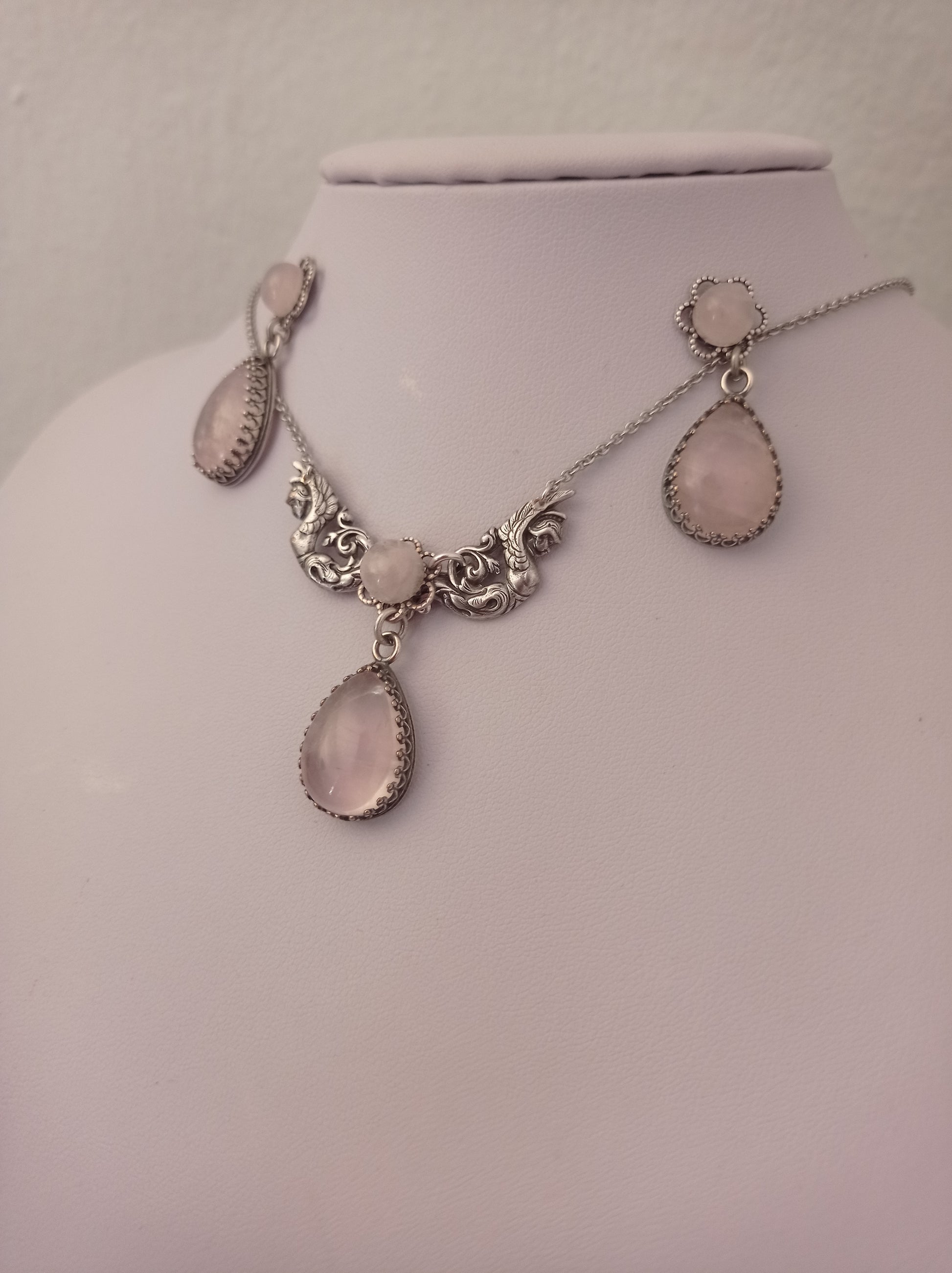 Rose Quartz necklace and earrings set featuring ornate detailing and matching pink teardrop-shaped stones. The set includes drop earrings and a necklace with three stones in decorative frames.