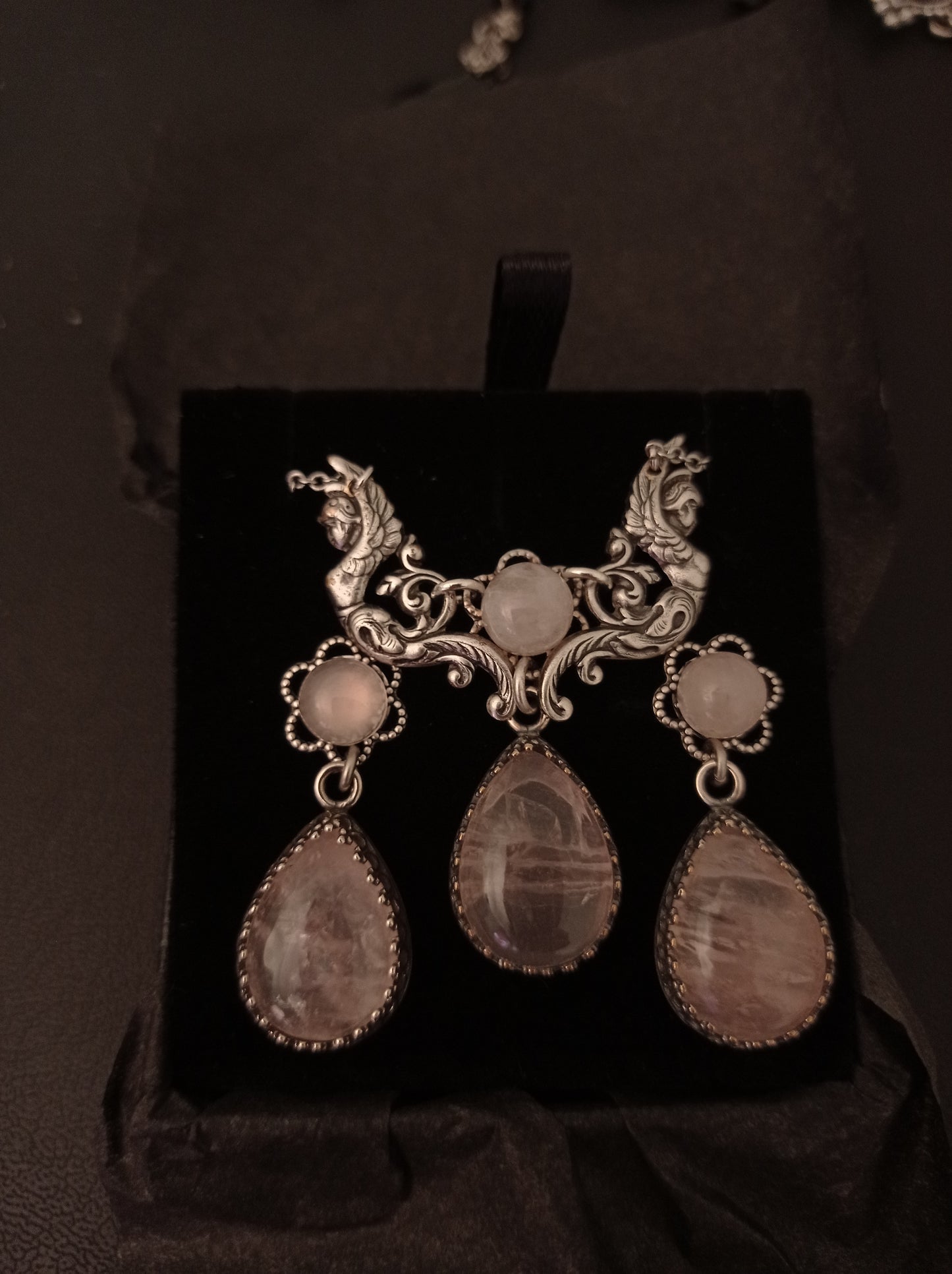 Ornate silver earrings with teardrop-shaped rose Quartz gemstones on a black stand.