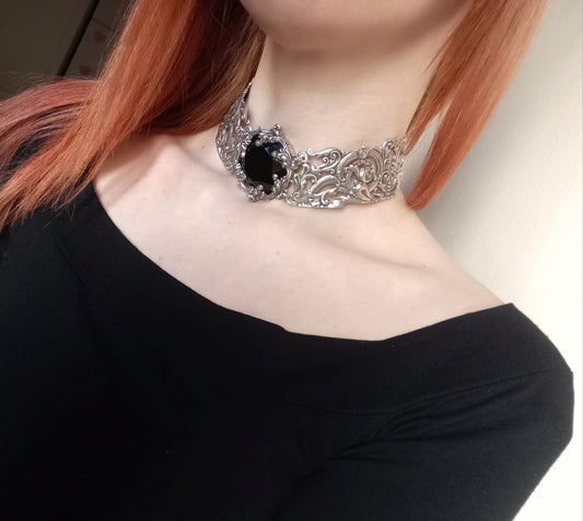 Black gothic choker. Silver collar with intricate flourishes across its length and a round black crystal jewel in the front.
