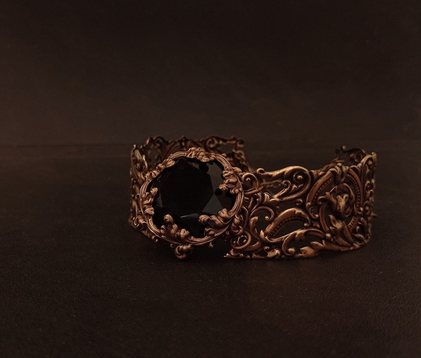 Intricately detailed wide brass Victorian Gothic choker featuring a large black gemstone at its center, resting on a dark textured surface.
