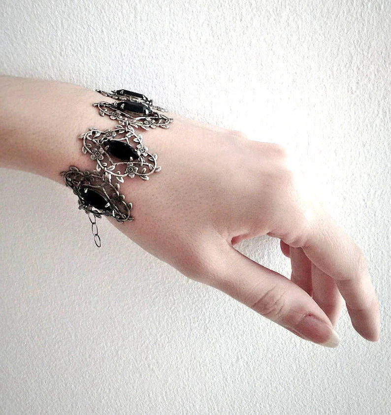 A sterling silver plated brass bracelet featuring filigree leaves with jet black Swarovski crystals creating a lace sleeve effect.