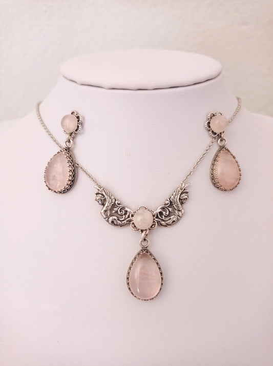 Victorian Rose Quartz necklace and earrings set featuring ornate detailing and matching pink teardrop-shaped stones. The set includes drop earrings and a necklace with three stones in decorative frames.