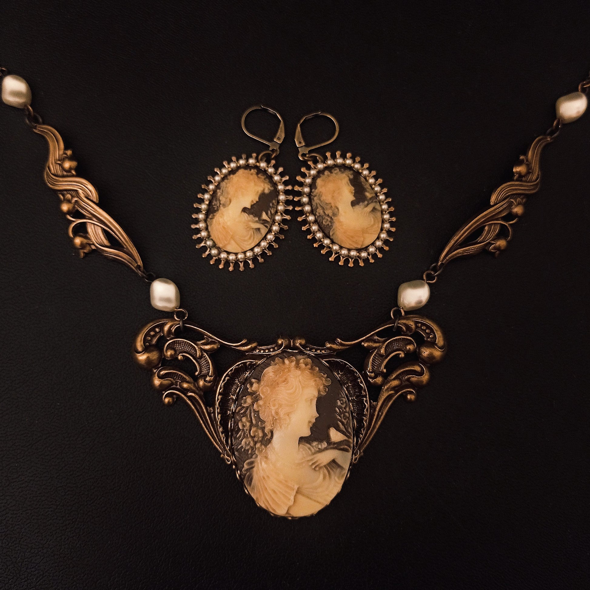 A Victorian jewelry set of bronze-toned necklace and matching earrings featuring ivory cameos of a woman me, framed with ornate scrollwork and pearl accents. Gothic Victorian jewelry, vintage jewelry 