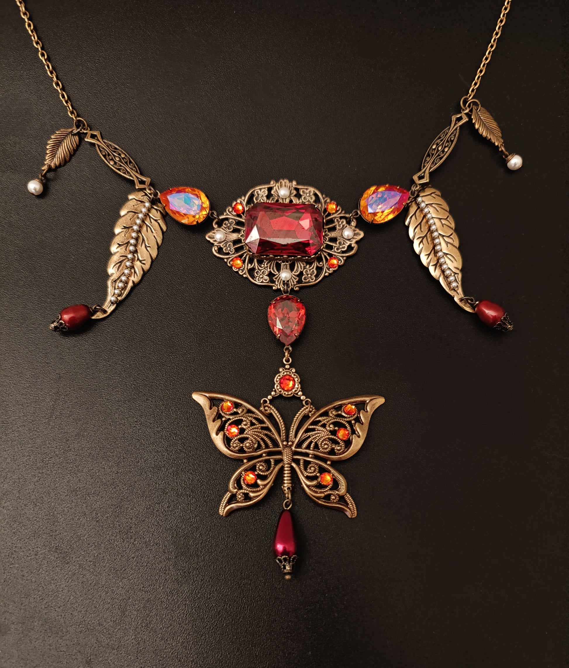 Fiery orange/red Austrian crystals come together with a large brass filigree butterfly and delicate white pearls in this necklace! 