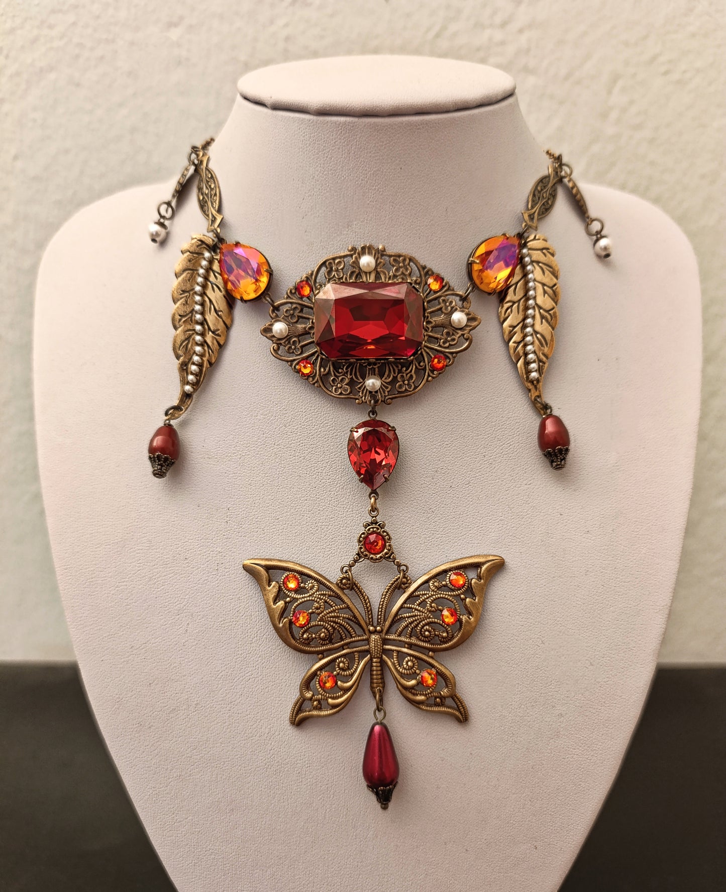 Ornate necklace with butterfly pendant and red gemstones on a mannequin bust.