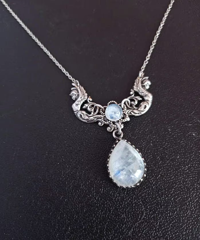 A Vintage inspired necklace with a silver-colored centerpiece featuring two winged female forms and two moonstone cabochons.