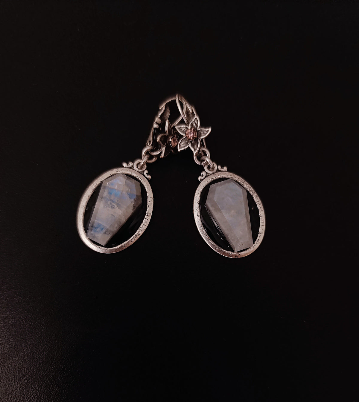 A pair of silver drop earrings with oval bezel settings holding milky white moostones with subtle blue-gray flashes, displayed on a dark black background.
