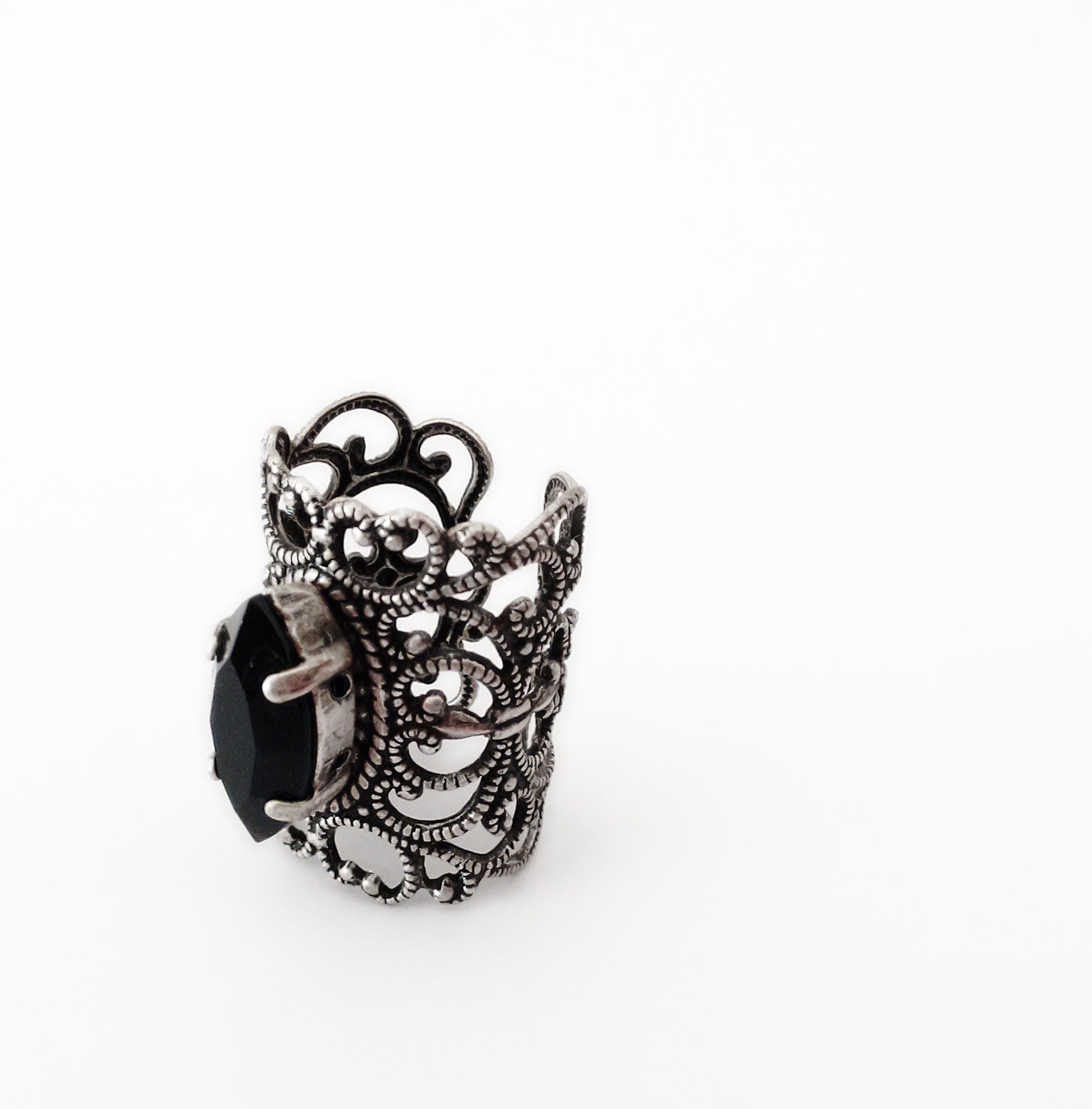 A decorative silver knuckle ring with intricate filigree design, featuring a prominent black marquise gemstone set at the center.

