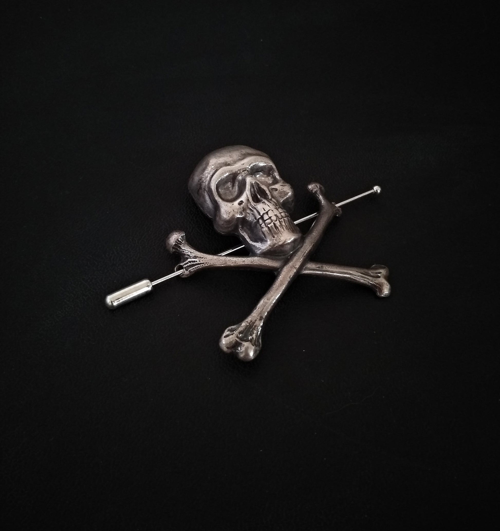 A large sterling silver plated gothic brooch featuring a skull and crossbones design.